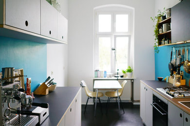 Geschlossene, Zweizeilige, Mittelgroße Moderne Küche ohne Insel mit integriertem Waschbecken, flächenbündigen Schrankfronten, grauen Schränken, Küchenrückwand in Blau, schwarzen Elektrogeräten, Linoleum, schwarzem Boden und schwarzer Arbeitsplatte in Berlin
