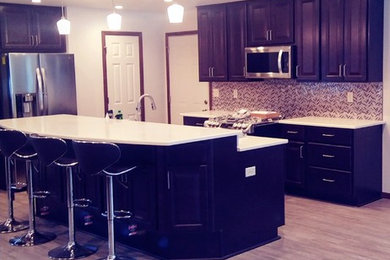 Contemporary u-shaped open plan kitchen in Milwaukee with an undermount sink, raised-panel cabinets, dark wood cabinets, quartzite benchtops, mosaic tile splashback, stainless steel appliances, laminate floors, with island, grey floor and white benchtop.