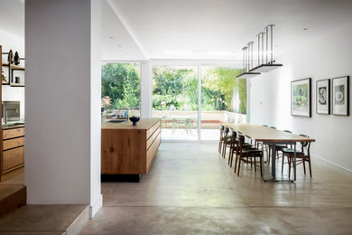 This is an example of a large contemporary single-wall kitchen/diner in London with a built-in sink, flat-panel cabinets, wood worktops, metal splashback, stainless steel appliances, concrete flooring, an island, a drop ceiling, feature lighting and medium wood cabinets.