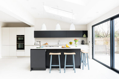 Photo of a mid-sized contemporary kitchen in London with an integrated sink, flat-panel cabinets, quartzite benchtops, white splashback, black appliances, terra-cotta floors, with island, white floor and white benchtop.