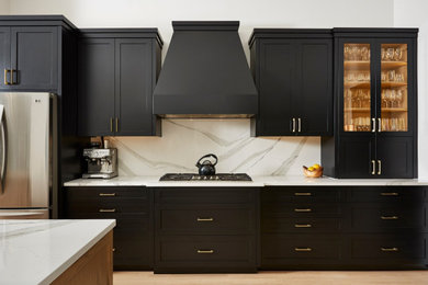 Example of a mid-sized transitional single-wall light wood floor and brown floor eat-in kitchen design in Minneapolis with a farmhouse sink, recessed-panel cabinets, black cabinets, quartz countertops, white backsplash, quartz backsplash, stainless steel appliances, an island and white countertops