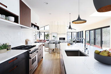 Design ideas for a mid-sized contemporary l-shaped open plan kitchen in Indianapolis with an undermount sink, flat-panel cabinets, black cabinets, quartz benchtops, white splashback, stainless steel appliances, medium hardwood floors, with island, brown floor and white benchtop.