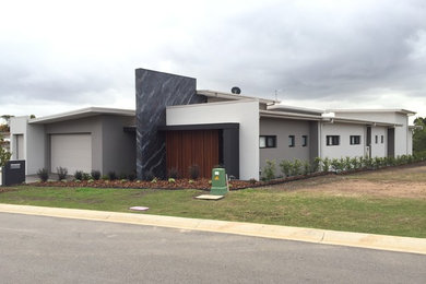 Photo of a large contemporary one-storey stucco grey house exterior in Newcastle - Maitland with a flat roof and a metal roof.