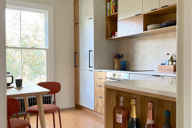Inspiration for a small retro l-shaped enclosed kitchen in London with an integrated sink, flat-panel cabinets, medium wood cabinets, composite countertops, beige splashback, stainless steel appliances, cork flooring, no island, brown floors, white worktops and feature lighting.