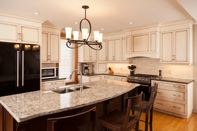 Mid-sized elegant l-shaped medium tone wood floor and brown floor open concept kitchen photo in Toronto with recessed-panel cabinets, distressed cabinets, an island, white backsplash, black appliances, a double-bowl sink, granite countertops and porcelain backsplash
