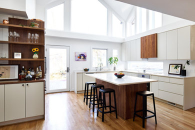 Kitchen - large 1950s u-shaped light wood floor and brown floor kitchen idea in DC Metro with an undermount sink, flat-panel cabinets, white cabinets, white backsplash, stainless steel appliances, an island and white countertops