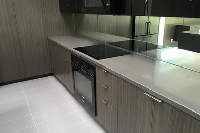 Inspiration for a mid-sized modern u-shaped porcelain tile and gray floor open concept kitchen remodel in Other with flat-panel cabinets, gray cabinets, solid surface countertops, multicolored backsplash, mirror backsplash, black appliances, an island and gray countertops