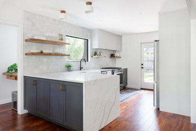 Inspiration for a mid-sized transitional l-shaped brown floor and medium tone wood floor eat-in kitchen remodel in Austin with a farmhouse sink, shaker cabinets, gray cabinets, quartz countertops, white backsplash, stainless steel appliances, a peninsula and white countertops