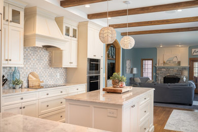 Design ideas for a mid-sized traditional u-shaped open plan kitchen in Minneapolis with a farmhouse sink, recessed-panel cabinets, white cabinets, quartzite benchtops, multi-coloured splashback, ceramic splashback, stainless steel appliances, medium hardwood floors, with island, brown floor, white benchtop and exposed beam.