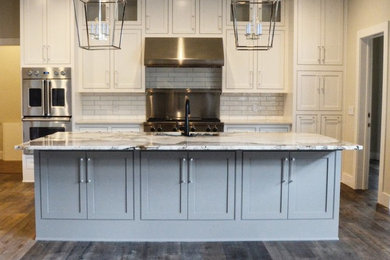 Example of a mid-sized transitional l-shaped medium tone wood floor and brown floor open concept kitchen design in Other with a double-bowl sink, shaker cabinets, white cabinets, granite countertops, white backsplash, subway tile backsplash, stainless steel appliances and an island