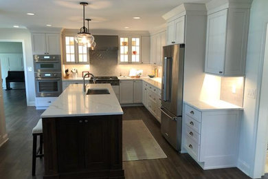 Enclosed kitchen - mid-sized traditional l-shaped light wood floor and beige floor enclosed kitchen idea in Philadelphia with a drop-in sink, flat-panel cabinets, white cabinets, marble countertops, beige backsplash, ceramic backsplash, stainless steel appliances, an island and white countertops