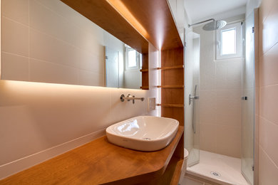 Cette image montre une petite douche en alcôve principale design en bois brun avec un placard à porte affleurante, WC suspendus, un carrelage blanc, des carreaux de céramique, un mur blanc, un lavabo posé, un plan de toilette en bois, un sol gris, une cabine de douche à porte battante et un plan de toilette marron.