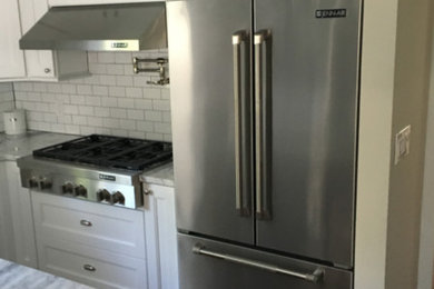 Large transitional u-shaped dark wood floor and brown floor enclosed kitchen photo in New York with a farmhouse sink, recessed-panel cabinets, white cabinets, marble countertops, white backsplash, subway tile backsplash, stainless steel appliances and an island