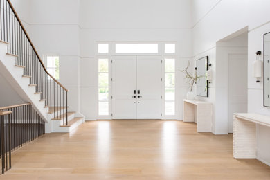 Large transitional light wood floor, brown floor, vaulted ceiling and wood wall entryway photo in New York with white walls and a white front door