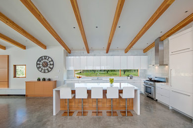 This is an example of a contemporary l-shaped kitchen in Vancouver with an undermount sink, flat-panel cabinets, white cabinets, white splashback, panelled appliances, concrete floors and with island.