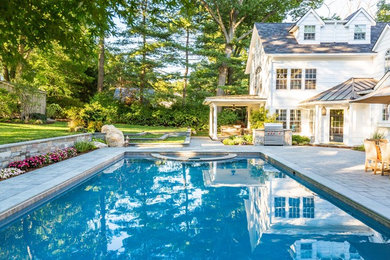 This is an example of a large modern backyard rectangular natural pool in New York with a hot tub and natural stone pavers.