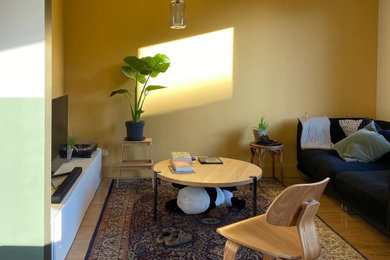 Idées déco pour un petit salon éclectique ouvert avec un mur jaune, parquet clair, aucune cheminée, un téléviseur indépendant et canapé noir.