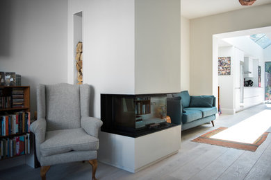 This is an example of a mid-sized contemporary formal open concept living room in London with white walls, medium hardwood floors, a wood stove, a plaster fireplace surround, a concealed tv and white floor.
