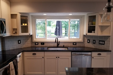 Kitchen - farmhouse l-shaped vinyl floor and gray floor kitchen idea in Cleveland with an undermount sink, shaker cabinets, white cabinets, gray backsplash, glass tile backsplash, stainless steel appliances, an island and black countertops
