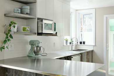 Inspiration for a mid-sized contemporary l-shaped porcelain tile kitchen remodel in Ottawa with stainless steel countertops, an integrated sink, flat-panel cabinets, distressed cabinets, white backsplash, subway tile backsplash, stainless steel appliances and a peninsula