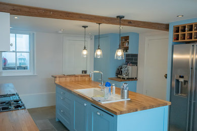 Design ideas for a bohemian kitchen in London with a double-bowl sink, shaker cabinets, blue cabinets, wood worktops, black splashback, ceramic splashback, stainless steel appliances, limestone flooring and an island.