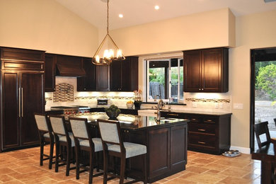 Example of a transitional l-shaped travertine floor eat-in kitchen design in Santa Barbara with an island, recessed-panel cabinets, wood countertops, beige backsplash, stone tile backsplash, paneled appliances and a farmhouse sink