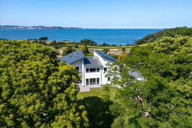 This is an example of a large and white contemporary detached house in Devon with three floors, a butterfly roof, a grey roof and a metal roof.