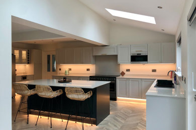 Design ideas for an expansive traditional l-shaped open plan kitchen in Glasgow with flat-panel cabinets, grey cabinets, quartz worktops, metallic splashback, stainless steel appliances, vinyl flooring, an island, white worktops and feature lighting.