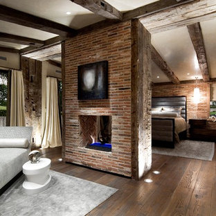 Design ideas for a large eclectic master bedroom in Orange County with beige walls, dark hardwood floors, a two-sided fireplace and a brick fireplace surround.