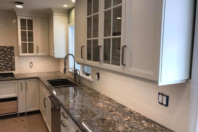 Mid-sized arts and crafts concrete floor and gray floor kitchen photo in New York with a double-bowl sink, recessed-panel cabinets, white cabinets, granite countertops, white backsplash, subway tile backsplash, stainless steel appliances and gray countertops