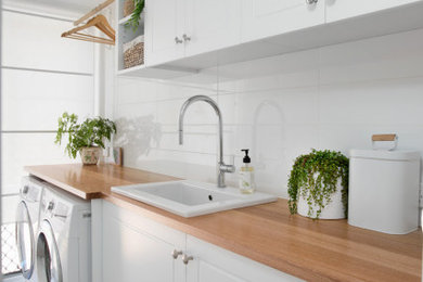 Inspiration for a dedicated laundry room in Brisbane with a single-bowl sink, shaker cabinets, white cabinets, wood benchtops, white walls, a side-by-side washer and dryer and grey floor.