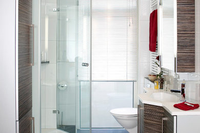 Kleines Modernes Duschbad mit flächenbündigen Schrankfronten, braunen Schränken, Wandtoilette mit Spülkasten, weißen Fliesen, weißer Wandfarbe, integriertem Waschbecken, Mineralwerkstoff-Waschtisch, schwarzem Boden und Falttür-Duschabtrennung in Frankfurt am Main