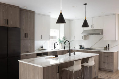 Example of a mid-sized minimalist l-shaped medium tone wood floor and brown floor open concept kitchen design in Seattle with a farmhouse sink, flat-panel cabinets, light wood cabinets, laminate countertops, white backsplash, stone slab backsplash, black appliances, an island and white countertops