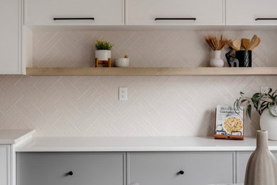 Kitchen - mid-sized modern l-shaped vinyl floor kitchen idea in Calgary with an undermount sink, flat-panel cabinets, white cabinets, quartz countertops, beige backsplash, ceramic backsplash, stainless steel appliances and an island