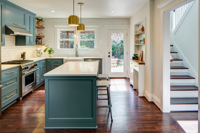 Photo of a transitional l-shaped kitchen in Portland with a farmhouse sink, recessed-panel cabinets, turquoise cabinets, white splashback, subway tile splashback, stainless steel appliances, medium hardwood floors, with island, brown floor and white benchtop.