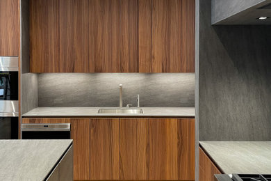 Idee per un'ampia cucina minimalista con lavello sottopiano, ante lisce, ante in legno scuro, paraspruzzi grigio, elettrodomestici da incasso, parquet chiaro e top grigio