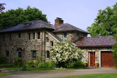 Mid-sized mediterranean two-storey house exterior in New York with stone veneer and a tile roof.