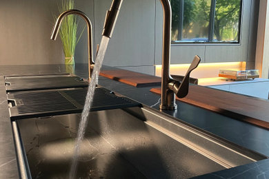 Inspiration for a mid-sized contemporary galley concrete floor eat-in kitchen remodel in Miami with an undermount sink, flat-panel cabinets, gray cabinets, solid surface countertops, black backsplash, ceramic backsplash, stainless steel appliances, an island and black countertops