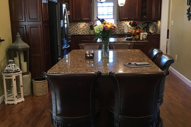Eat-in kitchen - large traditional u-shaped laminate floor eat-in kitchen idea in Philadelphia with an undermount sink, recessed-panel cabinets, dark wood cabinets, granite countertops, multicolored backsplash, mosaic tile backsplash, black appliances and two islands