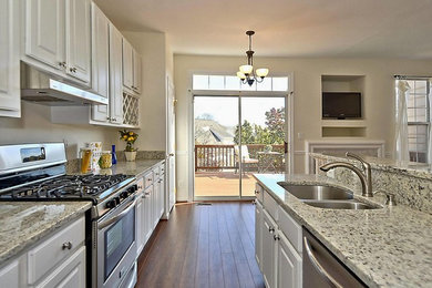 Large transitional galley dark wood floor open concept kitchen photo in DC Metro with a double-bowl sink, raised-panel cabinets, white cabinets, granite countertops, stone slab backsplash, stainless steel appliances and an island