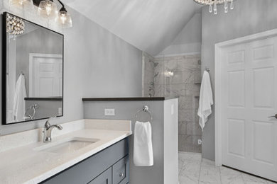 Modelo de cuarto de baño principal y doble con puertas de armario de madera en tonos medios, bañera exenta, lavabo bajoencimera, suelo gris y encimeras blancas