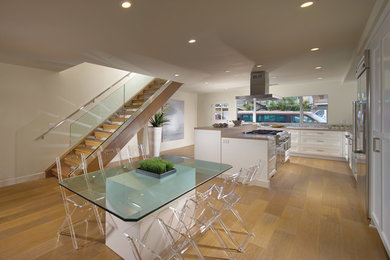 Example of a small trendy galley light wood floor eat-in kitchen design in Orange County with recessed-panel cabinets, white cabinets, solid surface countertops, beige backsplash, ceramic backsplash, stainless steel appliances and an island