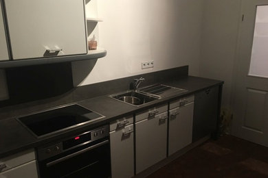 Photo of a small modern l-shaped enclosed kitchen in Other with a built-in sink, flat-panel cabinets, white cabinets, laminate countertops, grey splashback, wood splashback, stainless steel appliances, no island and grey worktops.