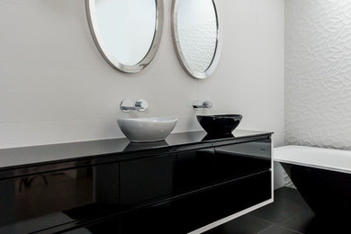 Large contemporary master bathroom in Auckland with furniture-like cabinets, black cabinets, a freestanding tub, a curbless shower, a one-piece toilet, black and white tile, porcelain tile, white walls, porcelain floors, a vessel sink and glass benchtops.