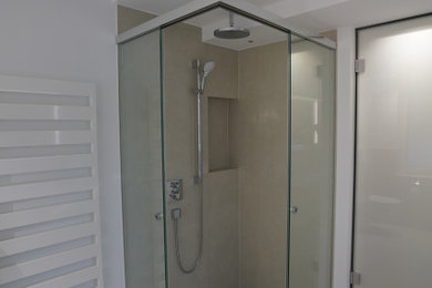 Foto på ett mellanstort funkis vit badrum med dusch, med släta luckor, vita skåp, en kantlös dusch, en vägghängd toalettstol, beige kakel, stenkakel, vita väggar, ett väggmonterat handfat, bänkskiva i glas, beiget golv och dusch med gångjärnsdörr