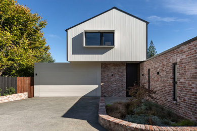 This is an example of a mid-sized contemporary two-storey brick white house exterior in Auckland with a gable roof, a metal roof, a black roof and board and batten siding.