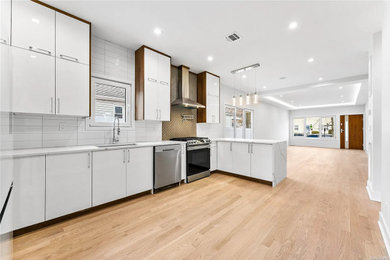 Large transitional l-shaped medium tone wood floor and brown floor kitchen photo in New York with a farmhouse sink, flat-panel cabinets, white cabinets, solid surface countertops, white backsplash, stone tile backsplash, black appliances, an island and white countertops