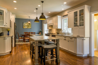 Photo of a mid-sized transitional u-shaped eat-in kitchen in Boston with an undermount sink, recessed-panel cabinets, white cabinets, granite benchtops, white splashback, ceramic splashback, stainless steel appliances, dark hardwood floors, with island, brown floor and multi-coloured benchtop.