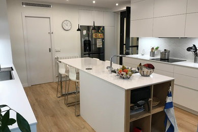 Modelo de cocina comedor lineal moderna grande con fregadero bajoencimera, armarios con paneles empotrados, puertas de armario blancas, encimera de cuarzo compacto, salpicadero blanco, electrodomésticos con paneles, suelo de madera en tonos medios, una isla y suelo marrón