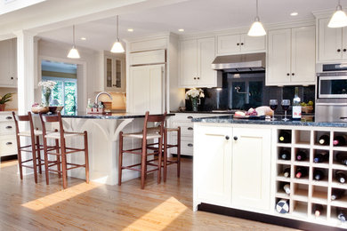 Example of a mid-sized transitional galley light wood floor and brown floor eat-in kitchen design in Other with an undermount sink, shaker cabinets, white cabinets, granite countertops, black backsplash, stone slab backsplash, stainless steel appliances and an island